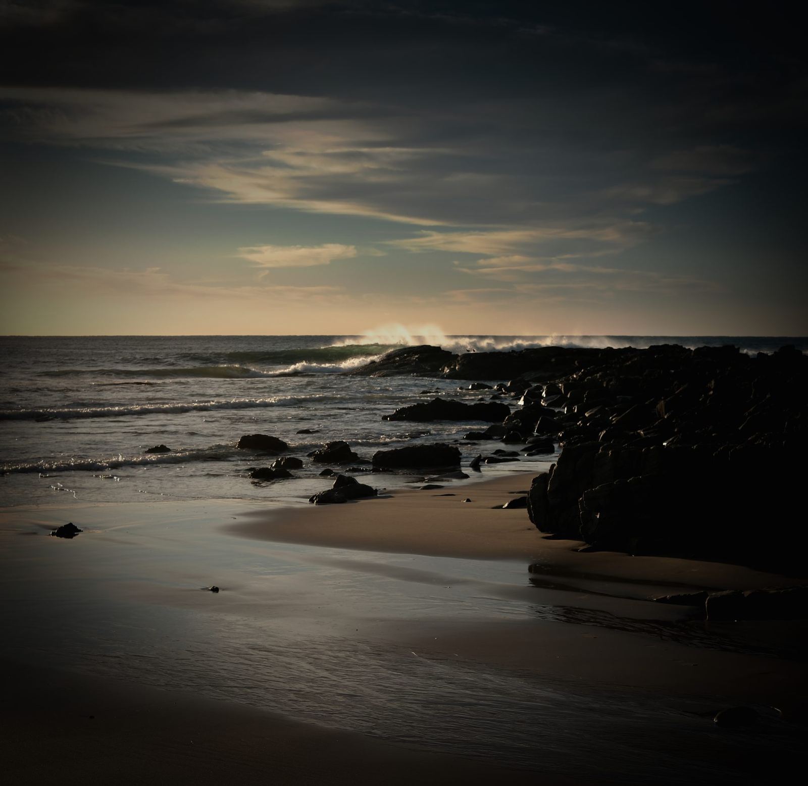 Dark rocks, breaking wave, dusk